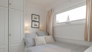 Une chambre à coucher avec un lit, deux lampes de chevet, une fenêtre avec des rideaux et deux tableaux encadrés accrochés au mur.
