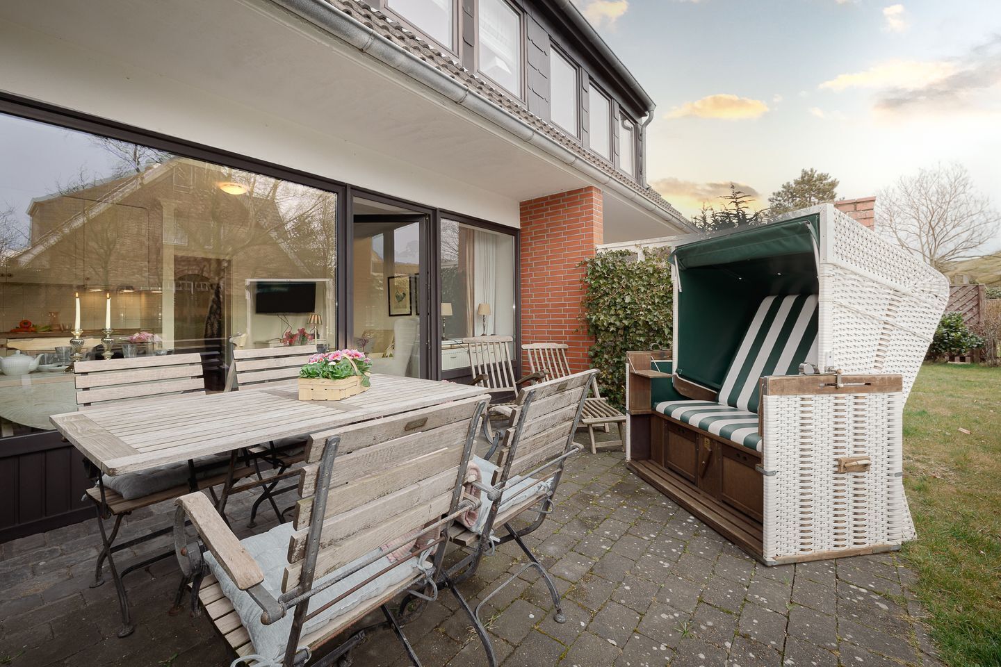 An outdoor patio with a wooden table and chairs, a wicker sofa, and a green cushioned seat.