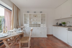 A kitchen with white cabinetry, a dining table set with plates and glasses, and a window with curtains.