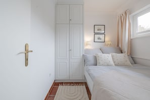 A bedroom with a bed, a wardrobe, a door with a handle, two wall-mounted lamps, and a window with curtains.