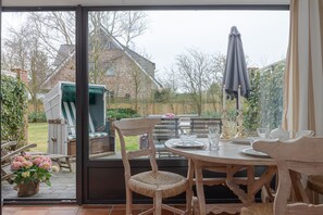 A patio with a table set for dining, wicker chairs, and a grill area visible through the glass door.