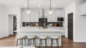 Una cocina moderna con una isla central, iluminación colgante y taburetes de bar.