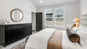 Un dormitorio con cama, cómoda, espejo y ventanas.