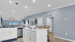 A modern kitchen with white cabinetry, a central island, and a dining area with chairs.