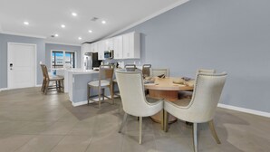 A modern kitchen with white cabinets, a central island, and a dining area with two upholstered chairs.