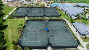 An aerial view of a sports complex with multiple tennis courts, surrounded by residential buildings and a swimming pool.