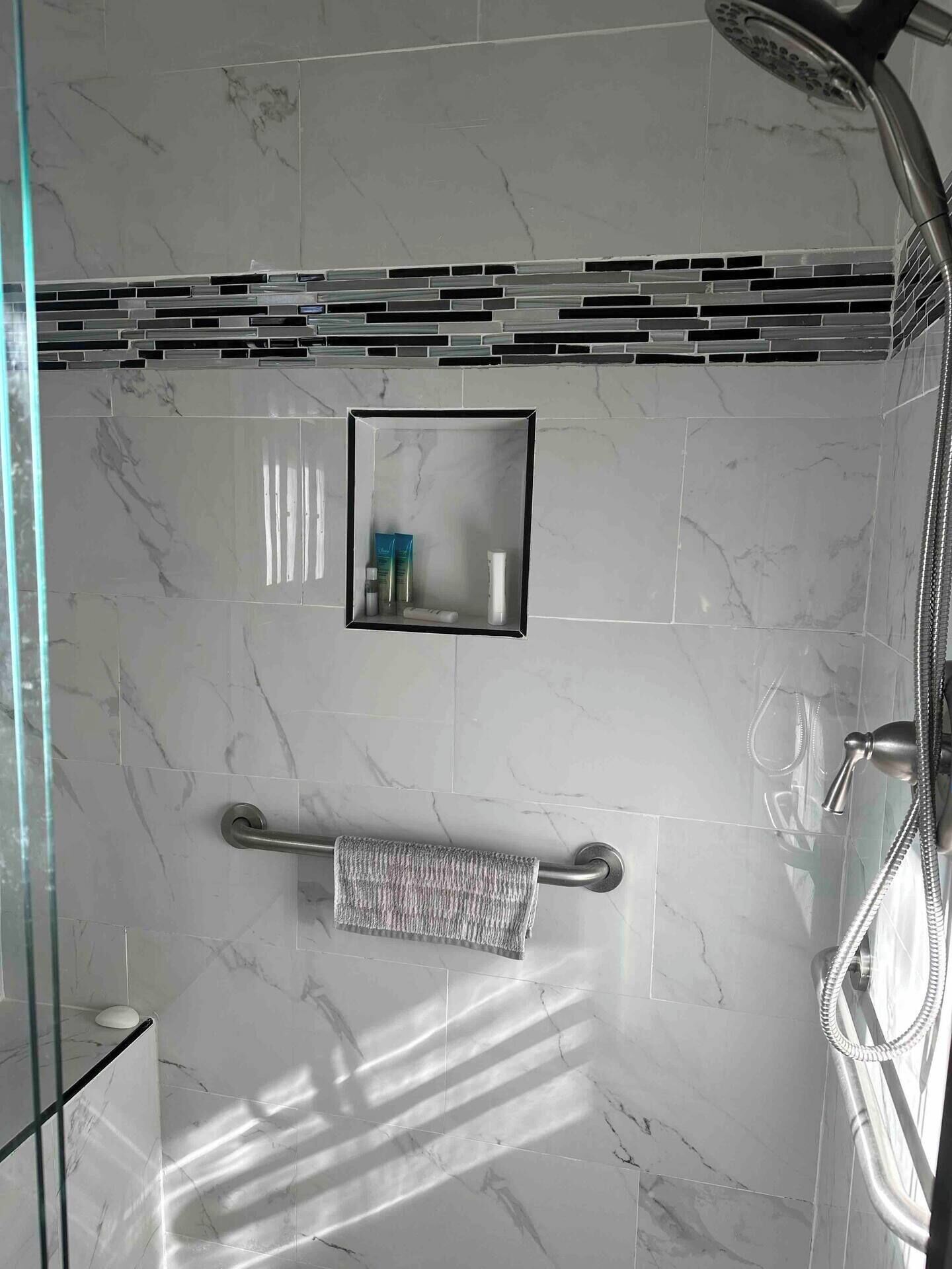 A modern bathroom with a glass shower enclosure, a towel rack, and a small mirror with toiletries.