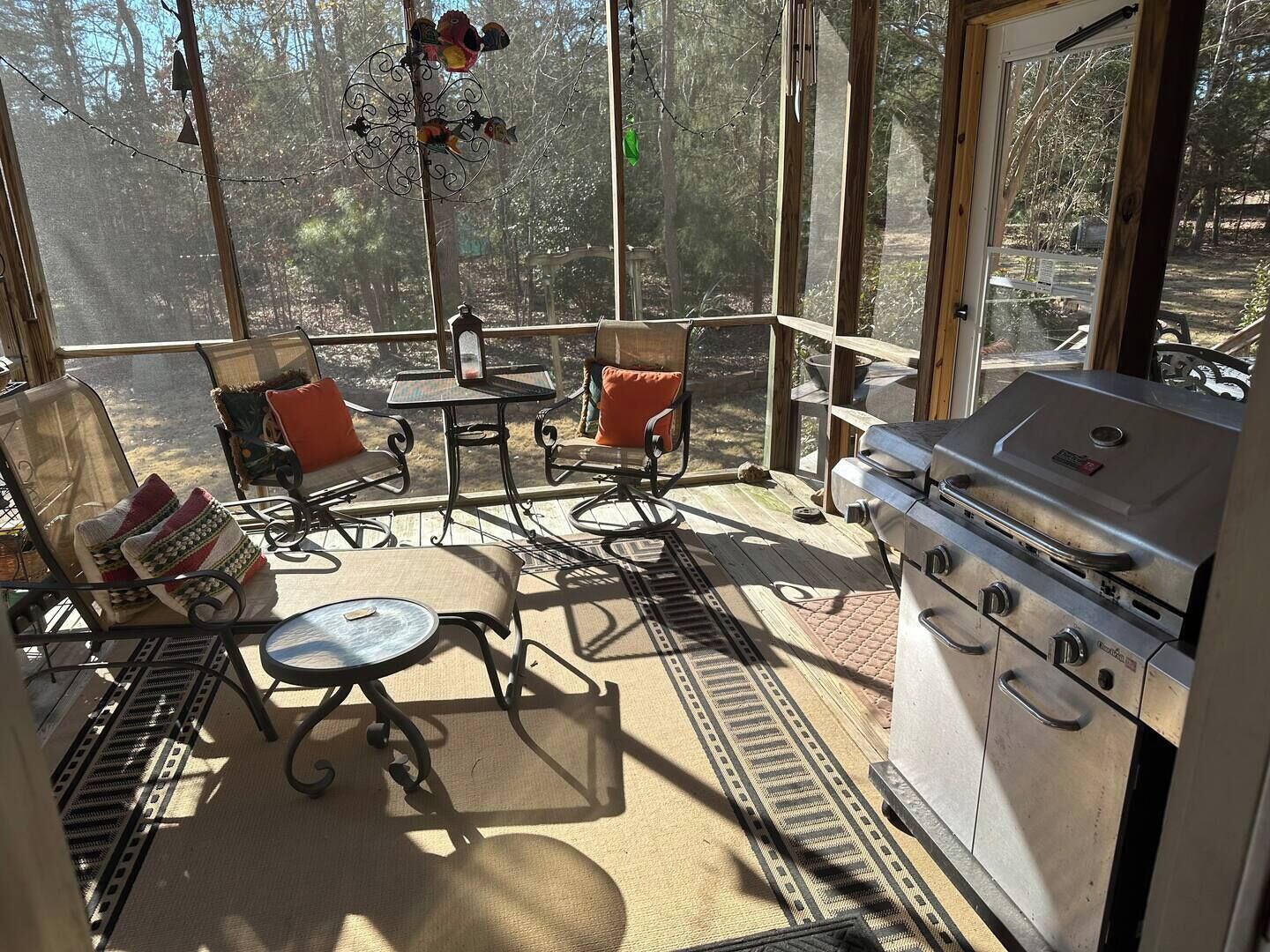Une terrasse ensoleillée avec un barbecue, des sièges d’extérieur et une vue sur la forêt.