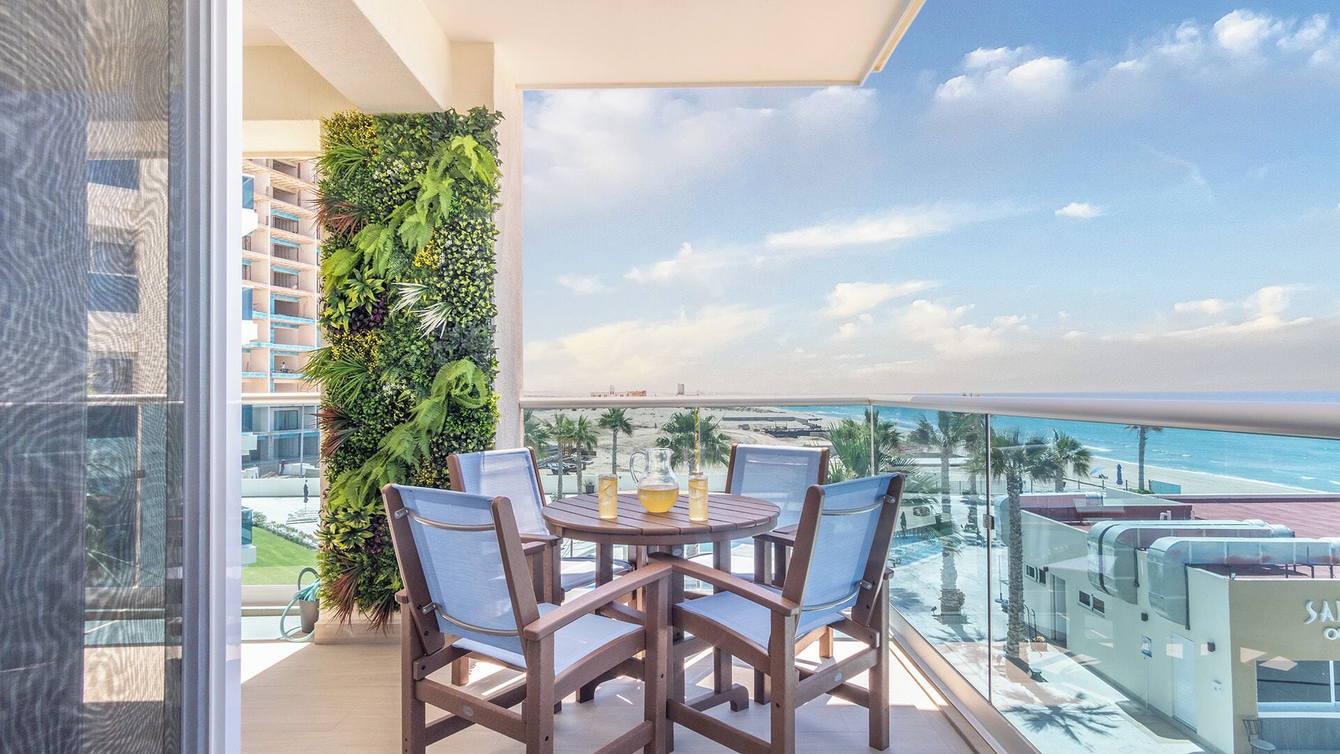 Un balcon avec vue sur la plage, un jardin vertical et une table avec des chaises.