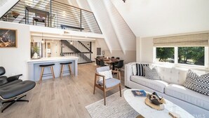 A spacious loft-style living area with a high ceiling, a dining area, and a staircase leading to an upper level. - Lake View Home, 2 Spacious Decks, Fire Pit, WiFi, On Sight Casita Option Avail. (Lake Arrowhead)