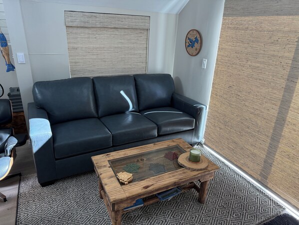 A living room with a black leather sofa, a wooden coffee table with decorative items, and a patterned rug.