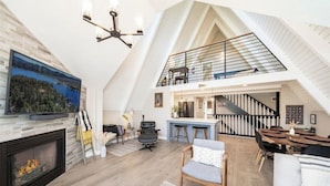 A spacious loft with a high ceiling, a fireplace, a dining area, and a kitchen. - Lake View Home, 2 Spacious Decks, Fire Pit, WiFi, On Sight Casita Option Avail. (Lake Arrowhead)