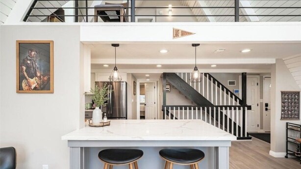 A modern kitchen with a central island, black bar stools, pendant lighting, and a staircase leading to an upper level. - Lake View Home, 2 Spacious Decks, Fire Pit, WiFi, On Sight Casita Option Avail. (Lake Arrowhead)