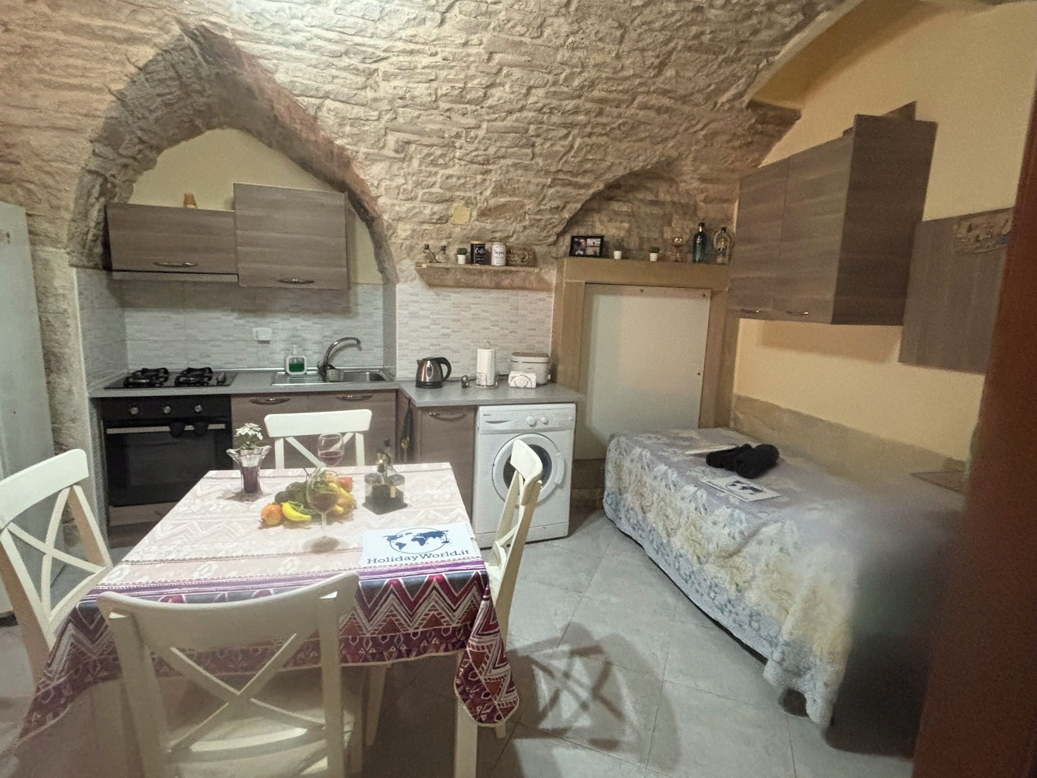 A compact kitchen with a dining area, a washing machine, and a bed.