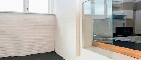 A corner of a room with a white brick wall, a black carpet, and a glass door leading to a kitchen area with a stove and microwave.