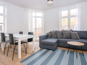A modern living room with a grey sofa, a small round table, and a dining table with chairs.