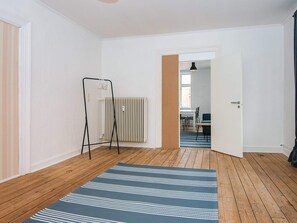 A room with a wooden floor, a blue striped rug, a radiator, and a door leading to a dining area.