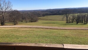 A view from a wooden deck overlooking a grassy field with trees and a distant hill. - Charming 1-bedroom house with WiFi and AC in peaceful Mount Pleasant (Mount Pleasant)