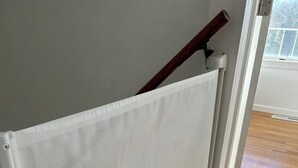 Una puerta mosquitera blanca de malla con un picaporte de madera, unida a un marco de puerta blanco, en una habitación con piso de madera.