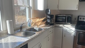 Una cocina moderna con armarios blancos, lavavajillas de acero inoxidable, cafetera, microondas y horno.