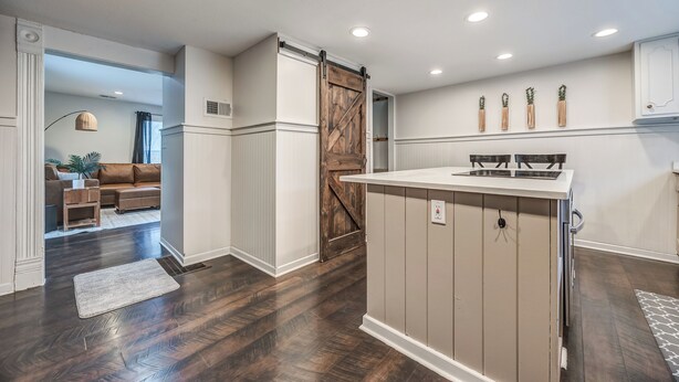 Una cocina moderna con una isla central, puerta de madera estilo granero y lámparas colgantes.