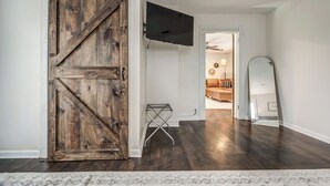 Una habitación con una puerta de madera estilo granero, un televisor montado, un tendedero de metal pequeño y un espejo grande.