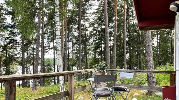 Een houten terras met twee stoelen en een tafel, met uitzicht op een bos en een waterpartij.
