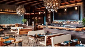 Un restaurant avec des tables et des chaises en bois, un coin bar et des lampes décoratives suspendues au plafond.