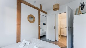 A modern hotel room with a large bed, a wooden beam structure, a round mirror, and a wardrobe. - Family home 2 steps from the Bassin (Gujan-Mestras)