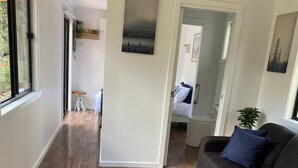 A spacious living area with a wooden floor, a grey sofa with blue cushions, and a small table with a plant. - Off grid tiny house bush escape (Nar Nar Goon North)