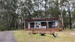 A cabin with a porch, wooden chairs, and a table. - Off grid tiny house bush escape (Nar Nar Goon North)