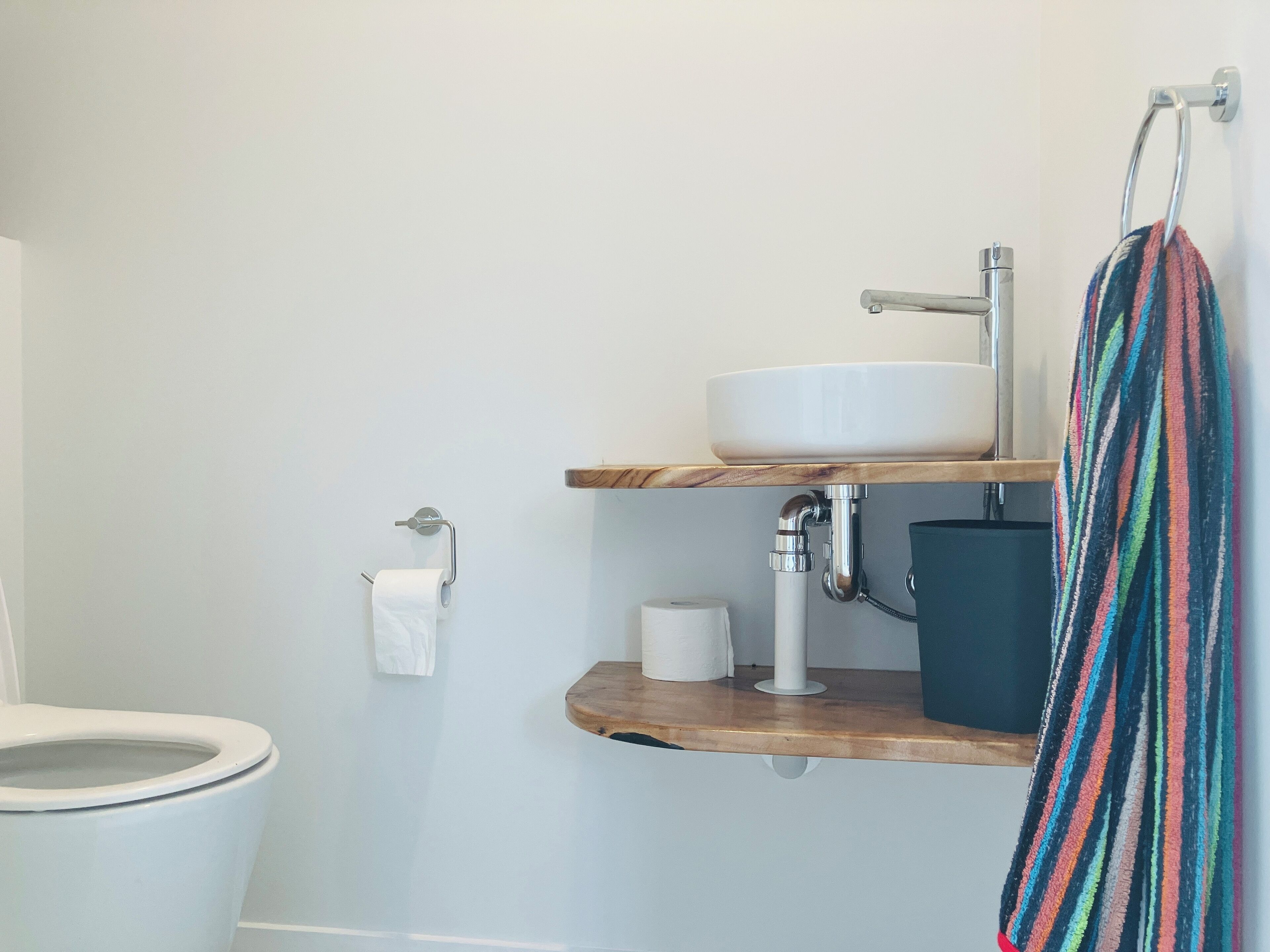 A bathroom with a toilet, a white sink, and a wooden shelf.