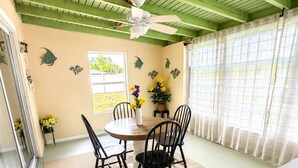 Un coin repas comprenant une table ronde, quatre chaises, un ventilateur de plafond et une fenêtre avec des rideaux.
