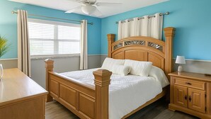 Une chambre à coucher avec un lit en bois, une table de chevet, un bureau et un ventilateur de plafond.