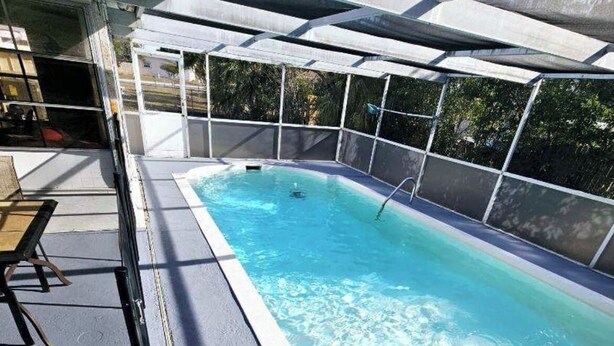 Une piscine extérieure rectangulaire à l’eau d’un bleu limpide, entourée d’une terrasse blanche et d’une clôture de sécurité en métal.