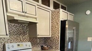 Une cuisine avec des meubles blancs, un réfrigérateur en acier inoxydable, un pare-feu en carrelage et un plancher en bois.