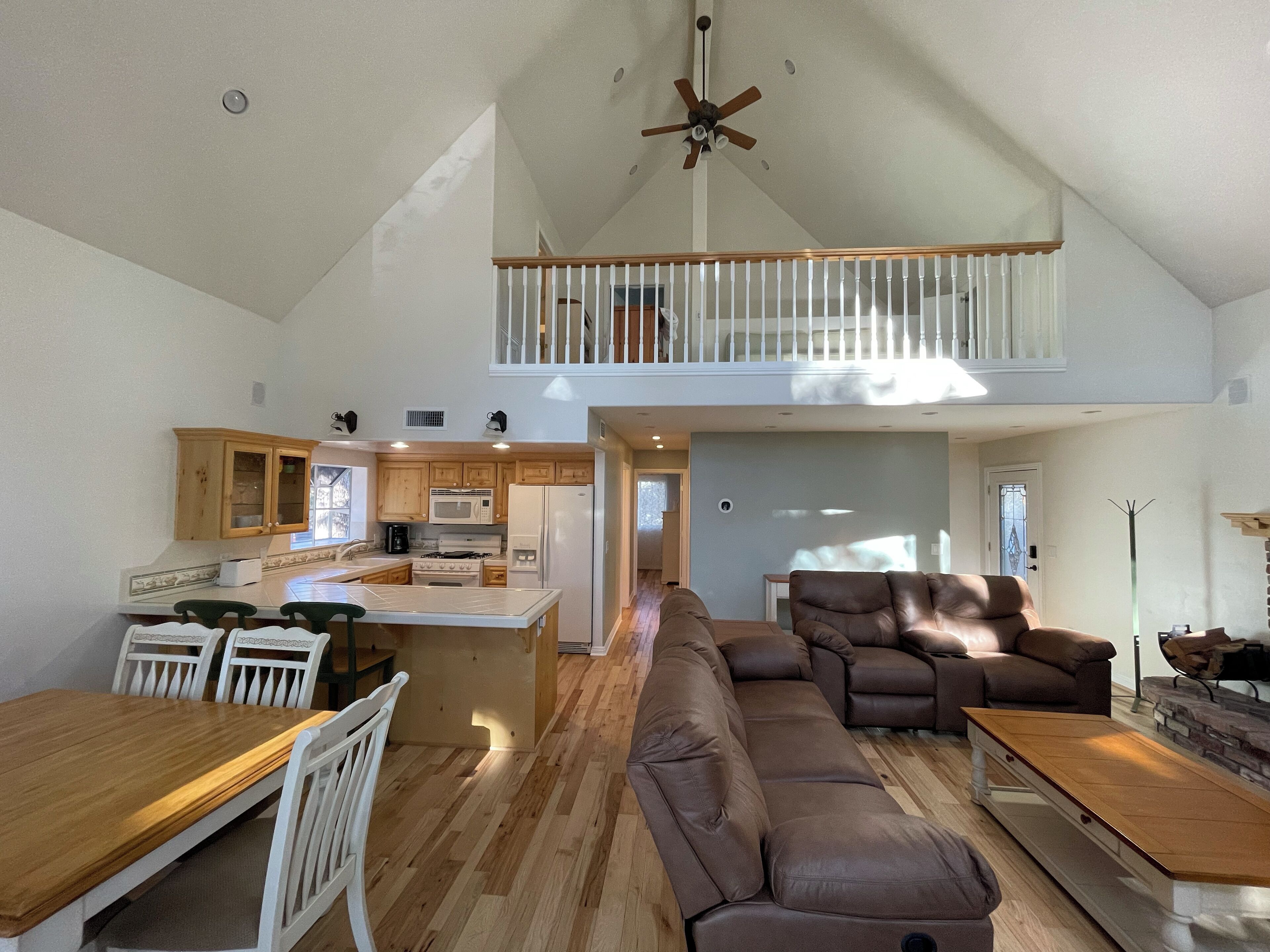 A spacious living area with a high ceiling, a dining table with chairs, a sofa, and a fireplace.