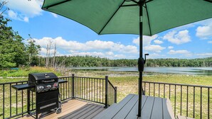 Een terras met een barbecue, een tafel en een groene parasol.