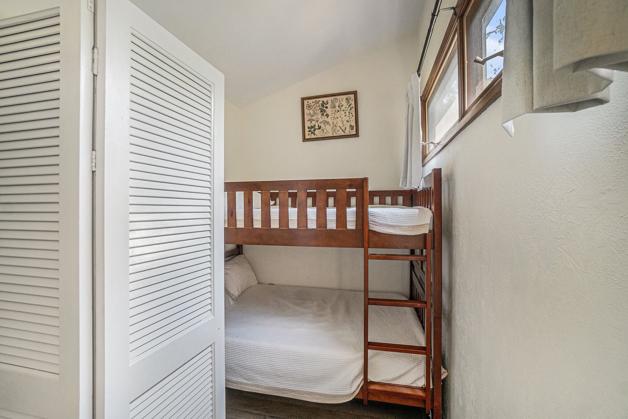 A bunk bed in a small room with a window, a door, and a framed picture on the wall.