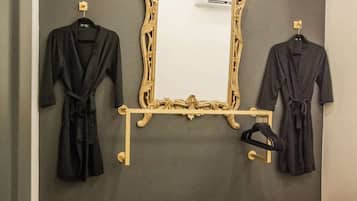 A bedroom with a dark wall, a large ornate mirror, and two black robes hanging on hooks.