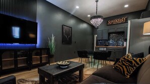 A modern living room with a flat-screen TV, a dining area with a chandelier, and a kitchen with a sign that reads "SPEAKASY." - "Speakeasy Suite" @ ArnoTriplex+Close to Dowtown+Pet Friendly! (Albuquerque)