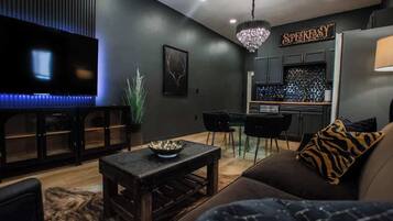 A modern living room with a flat-screen TV, a dining area with a chandelier, and a kitchen with a sign that reads "SPEAKASY."