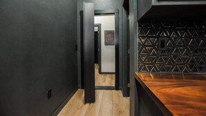 A narrow hallway with wooden flooring and dark walls, leading to a room with a geometric-patterned wall and a wooden counter. - "Speakeasy Suite" @ ArnoTriplex+Close to Dowtown+Pet Friendly! (Albuquerque)