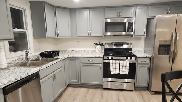A modern kitchen with grey cabinets, stainless steel appliances, a granite countertop, and a wooden floor.