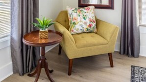 A room with a yellow armchair, a small wooden table with a plant, and a mirror on the wall.