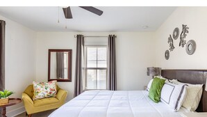 A bedroom with a bed, a chair, a table, a window, and wall decorations.
