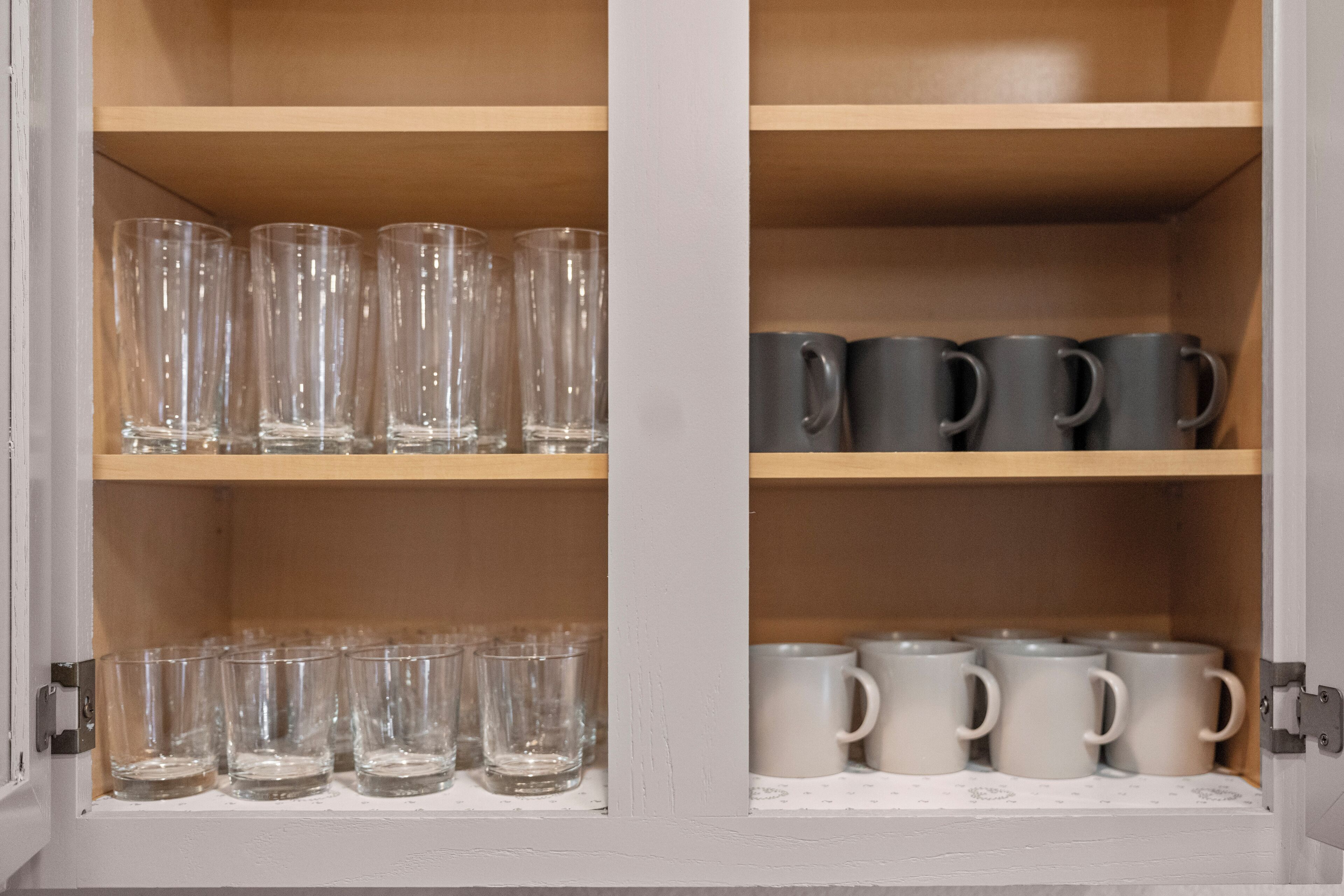 Ein Schrank mit Regalen, der klare Gläser, dunkle Tassen und weiße Tassen enthält.