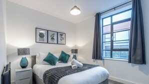 Un dormitorio moderno con cama, mesitas de noche, una lámpara y una ventana con cortinas.