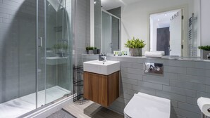 Un baño moderno con ducha acristalada, tocador de madera y un espejo grande.