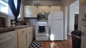 A compact kitchen with white cabinets, a white stove, and a refrigerator. There is a wooden floor and a patterned rug. - Comfy Rustic Retreat 2 blocks from Mayo Hospital and Bethany College. (Mankato)